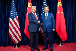 Donald Trump and Xi Jinping shake hands during a bilateral meeting with U.S. and Chinese flags in the background.
