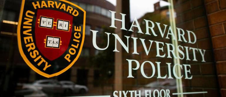 Harvard University Police Department headquarters window with the official shield and lettering reflected on a Cambridge building facade.