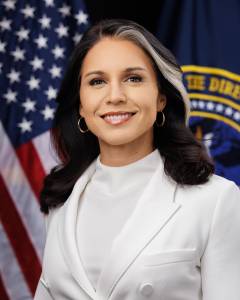 Official portrait of Director of National Intelligence Tulsi Gabbard wearing a white suit, standing in front of the American flag and the Office of the Director of National Intelligence emblem.