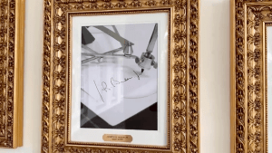 A framed photograph showing an autopen machine writing Joe Biden’s signature displayed in an ornate gold frame