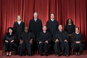 Official group portrait of the U S Supreme Court justices seated and standing in front of a red curtain