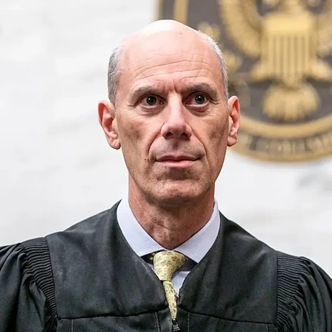 Portrait of Judge James E. Boasberg, Chief Judge of the U.S. District Court for the District of Columbia, standing in a courtroom with the U.S. judicial seal visible in the background.