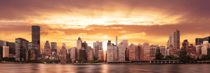 Panoramic view of the New York City skyline at sunset with orange and gold light over the East River.